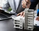 Mesa com uma maquete de um edifício com close nas mãos de duas pessoas conversando